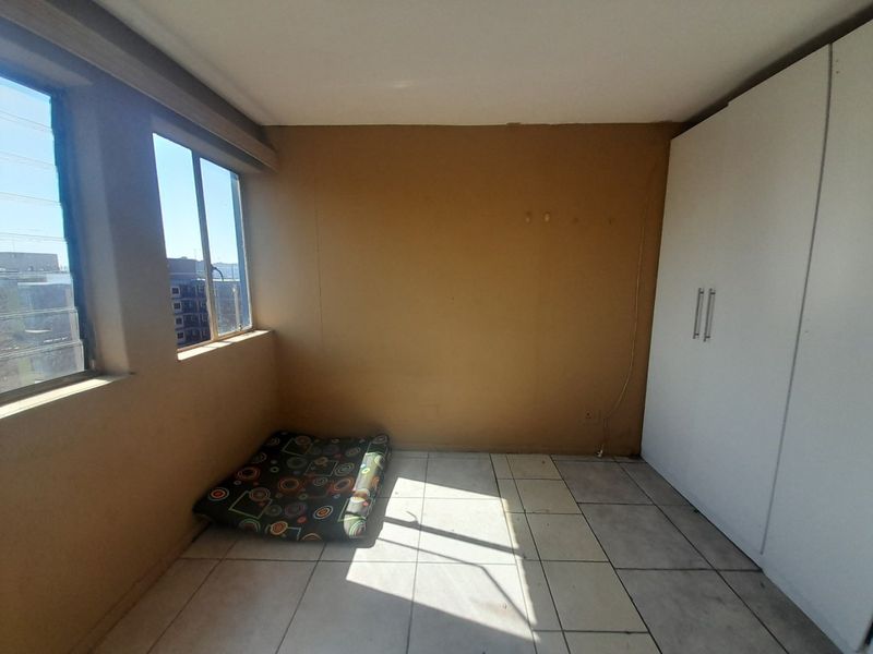 A simple bedroom featuring tiled flooring, louver windows, and a built-in white wardrobe, offering a blank canvas for potential updates.