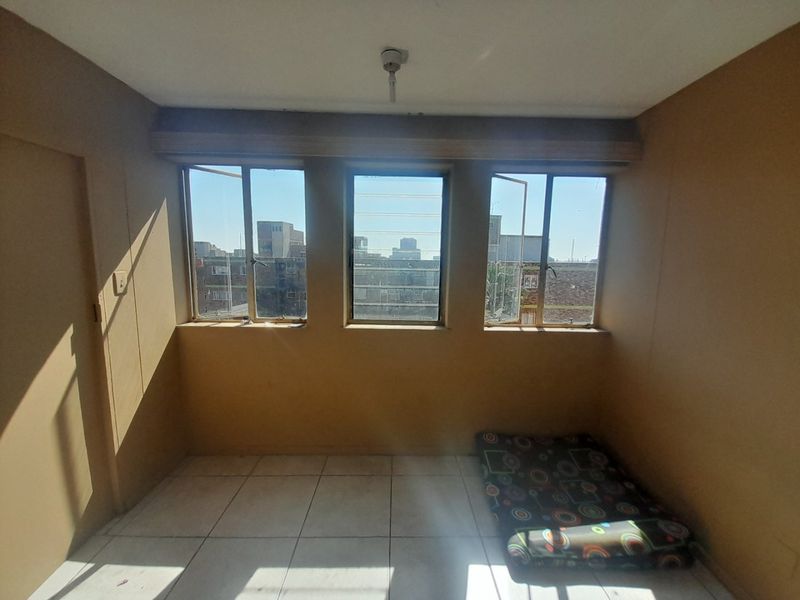 A vacant bedroom featuring tiled flooring and large windows with security bars, offering natural light and an urban view.