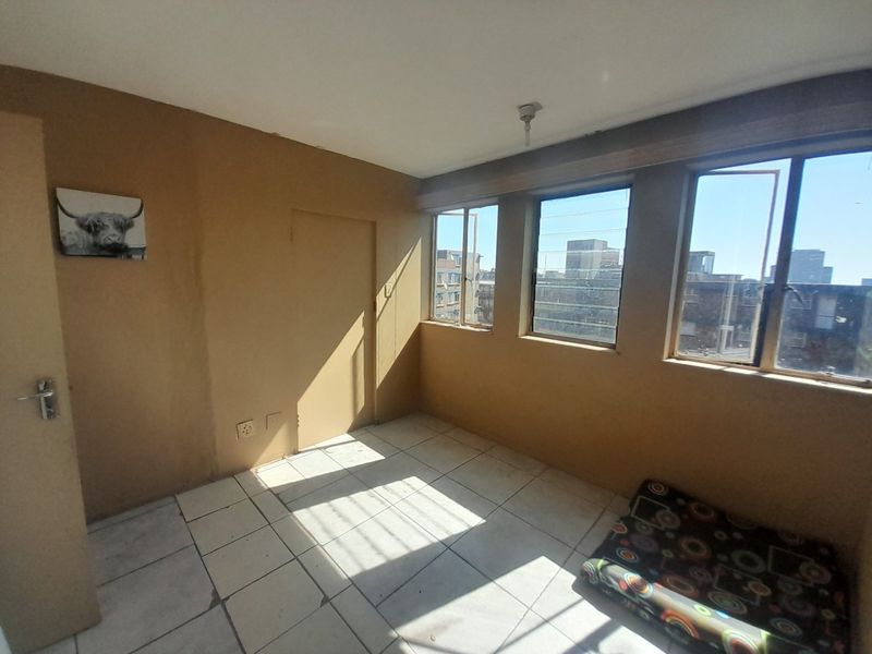 A vacant bedroom featuring tiled flooring and large windows providing natural light and urban views.