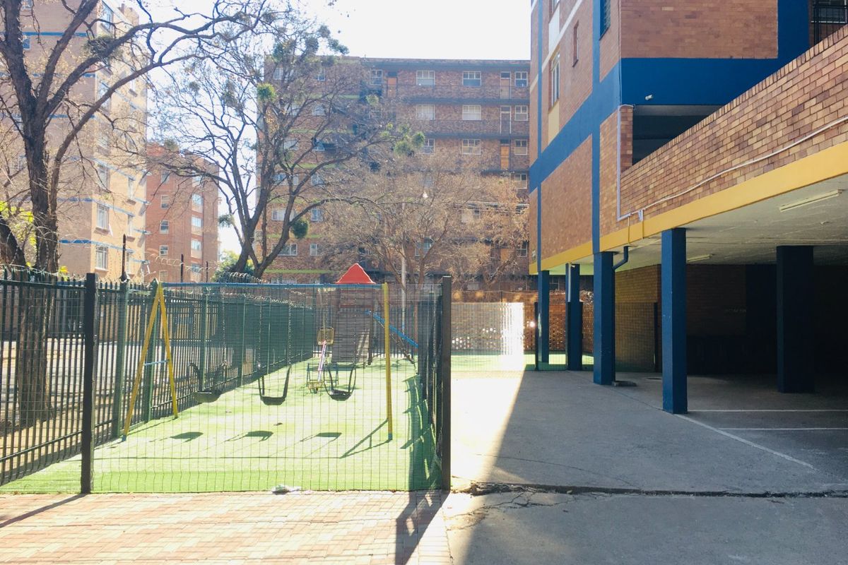 Exterior view of the apartment complex featuring a fenced playground area and covered parking facilities.