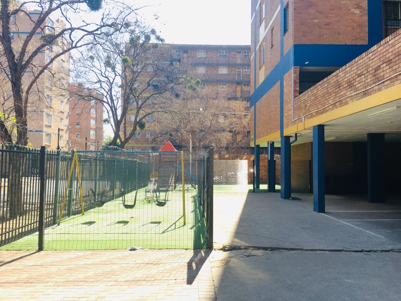 Exterior view of the apartment complex featuring a fenced playground area and covered parking facilities.