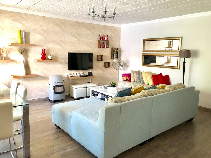 Spacious living room featuring laminate flooring, a textured feature wall, and a classic ceiling chandelier, creating a comfortable and inviting atmosphere.