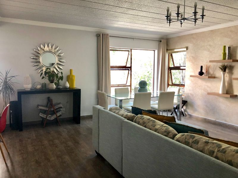 Spacious open-plan living and dining area featuring laminate flooring, a textured feature wall, floating shelves, and natural light through aluminium windows.