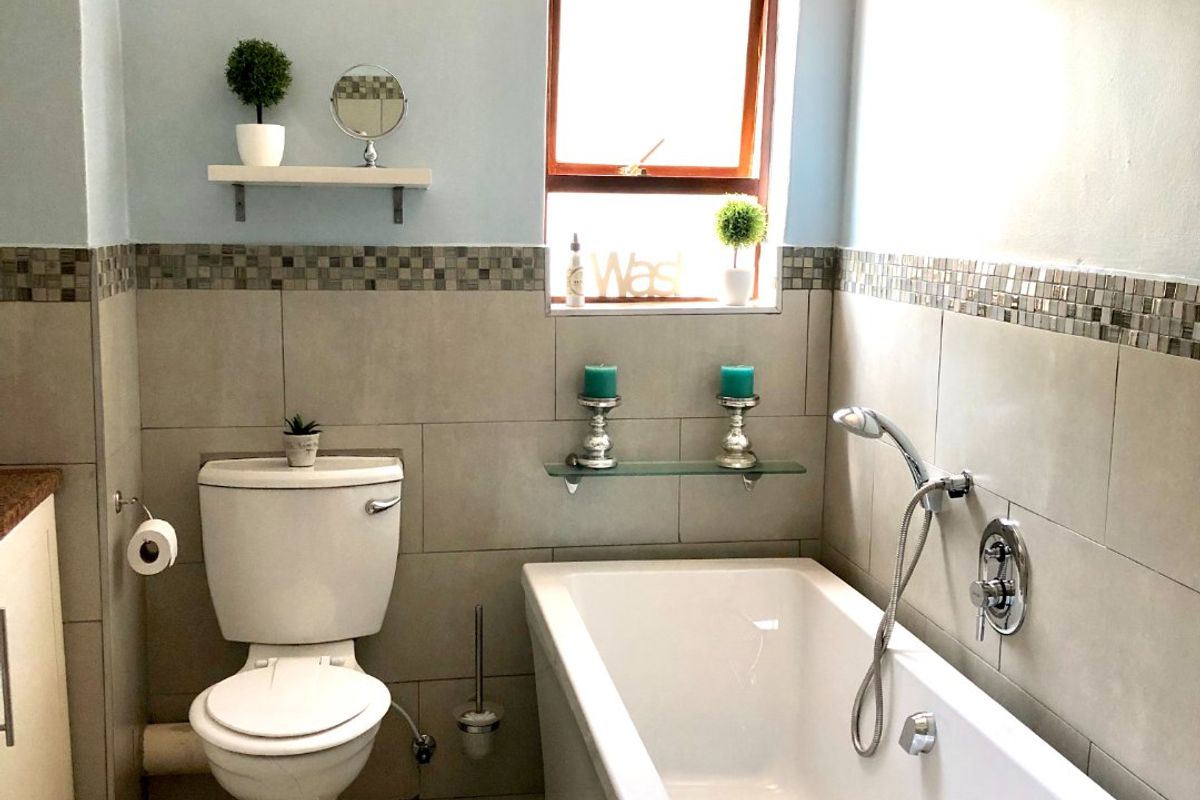 A well-maintained bathroom featuring a bathtub with a handheld shower mixer, a toilet, and neutral wall tiling with a decorative mosaic border.
