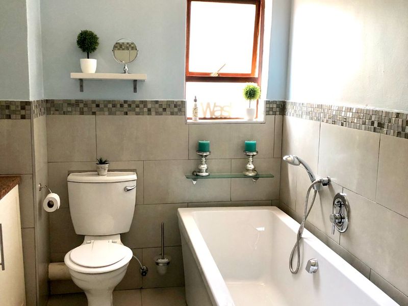 A well-maintained bathroom featuring a bathtub with a handheld shower mixer, a toilet, and neutral wall tiling with a decorative mosaic border.