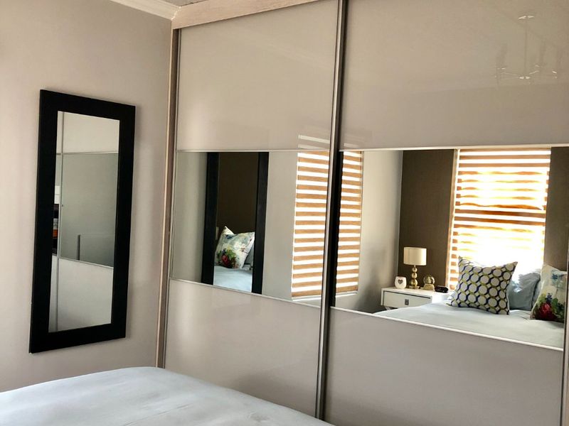 A well-maintained bedroom featuring a large built-in sliding door wardrobe with mirrored panels and modern venetian blinds.