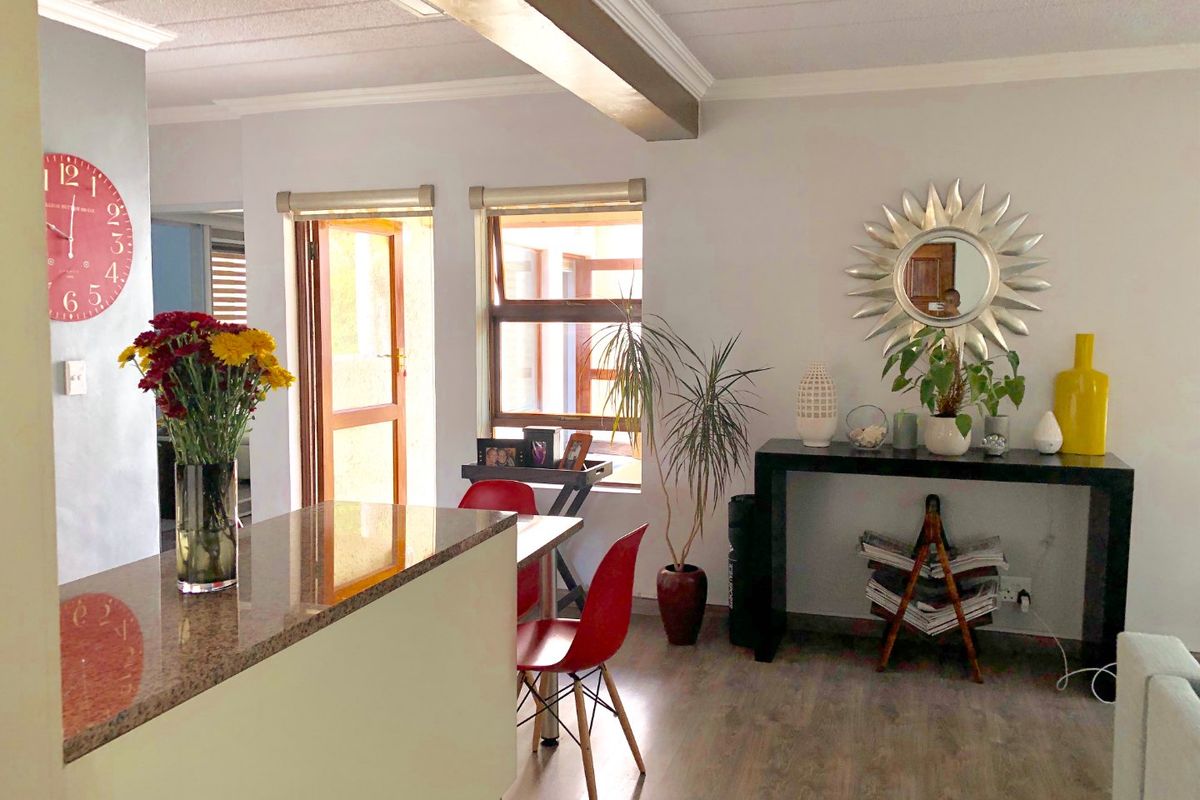 Open-plan living area featuring laminate flooring, a granite-topped breakfast counter, and natural light through timber-framed windows and doors.