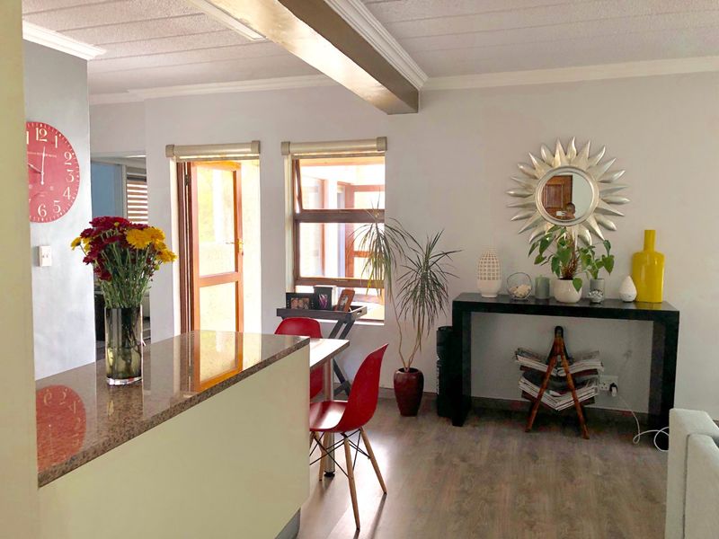 Open-plan living area featuring laminate flooring, a granite-topped breakfast counter, and natural light through timber-framed windows and doors.