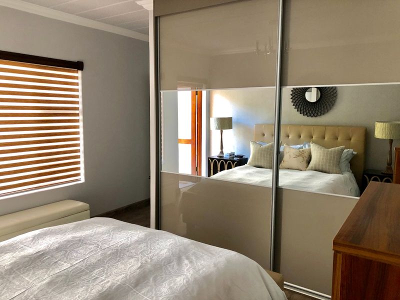 A well-maintained bedroom featuring a large built-in sliding door wardrobe with mirrored panels and modern venetian blinds.
