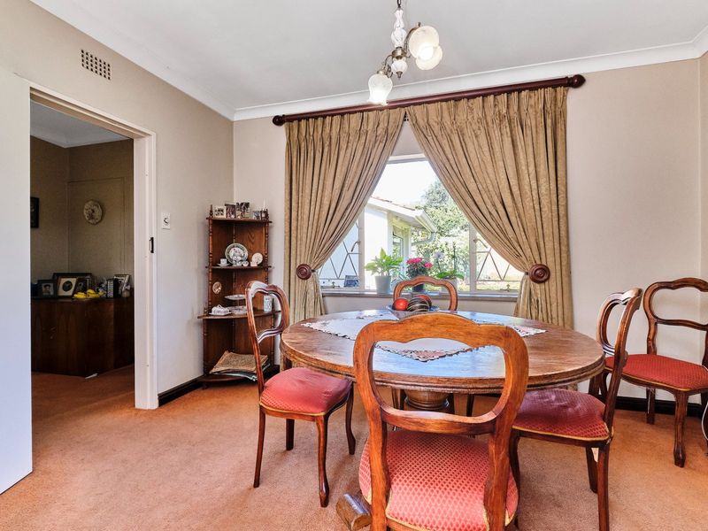 A traditional dining room featuring carpeted flooring, a central light fixture, and a window with curtains overlooking the exterior.
