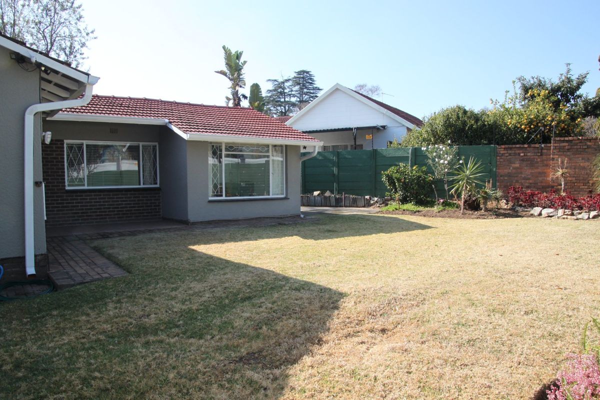 Rear view of the house featuring a lawn, paved walkway, and brick and painted exterior walls under a terracotta tiled roof.