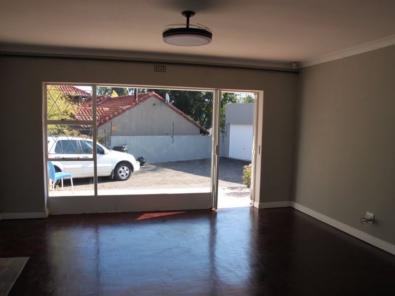 Spacious living room featuring polished parquet flooring, a ceiling fan, and large sliding glass doors providing direct access to the exterior driveway area.