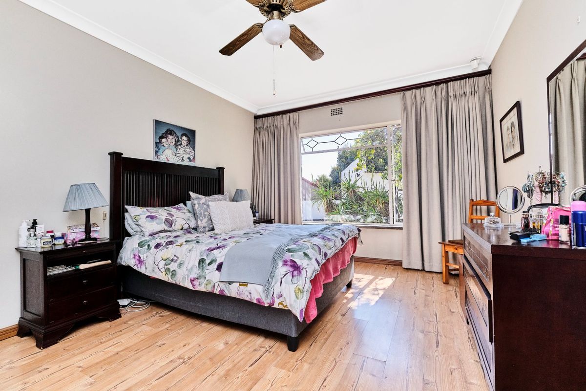 A spacious bedroom featuring timber flooring, a ceiling fan, and a large window allowing for natural light.