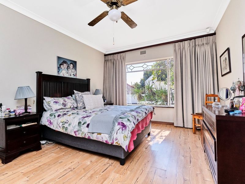 A spacious bedroom featuring timber flooring, a ceiling fan, and a large window allowing for natural light.
