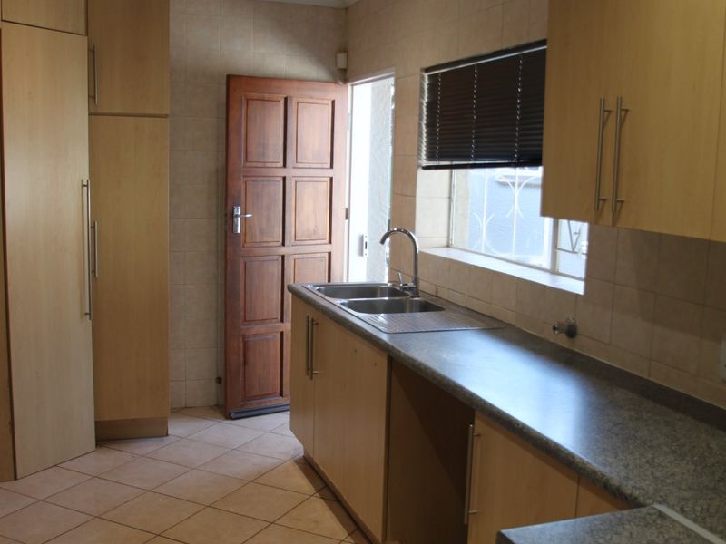 A functional kitchen featuring light wood cabinetry, granite-look laminate countertops, a double sink, and tiled flooring with direct access to the exterior.