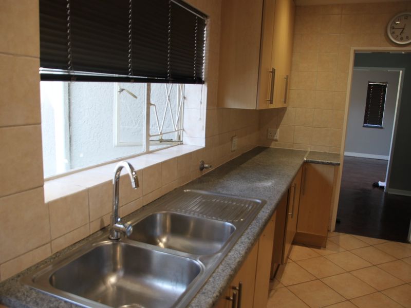 A functional kitchen featuring laminate cabinetry, stone-look countertops, a double stainless steel sink, and neutral ceramic tiling throughout.