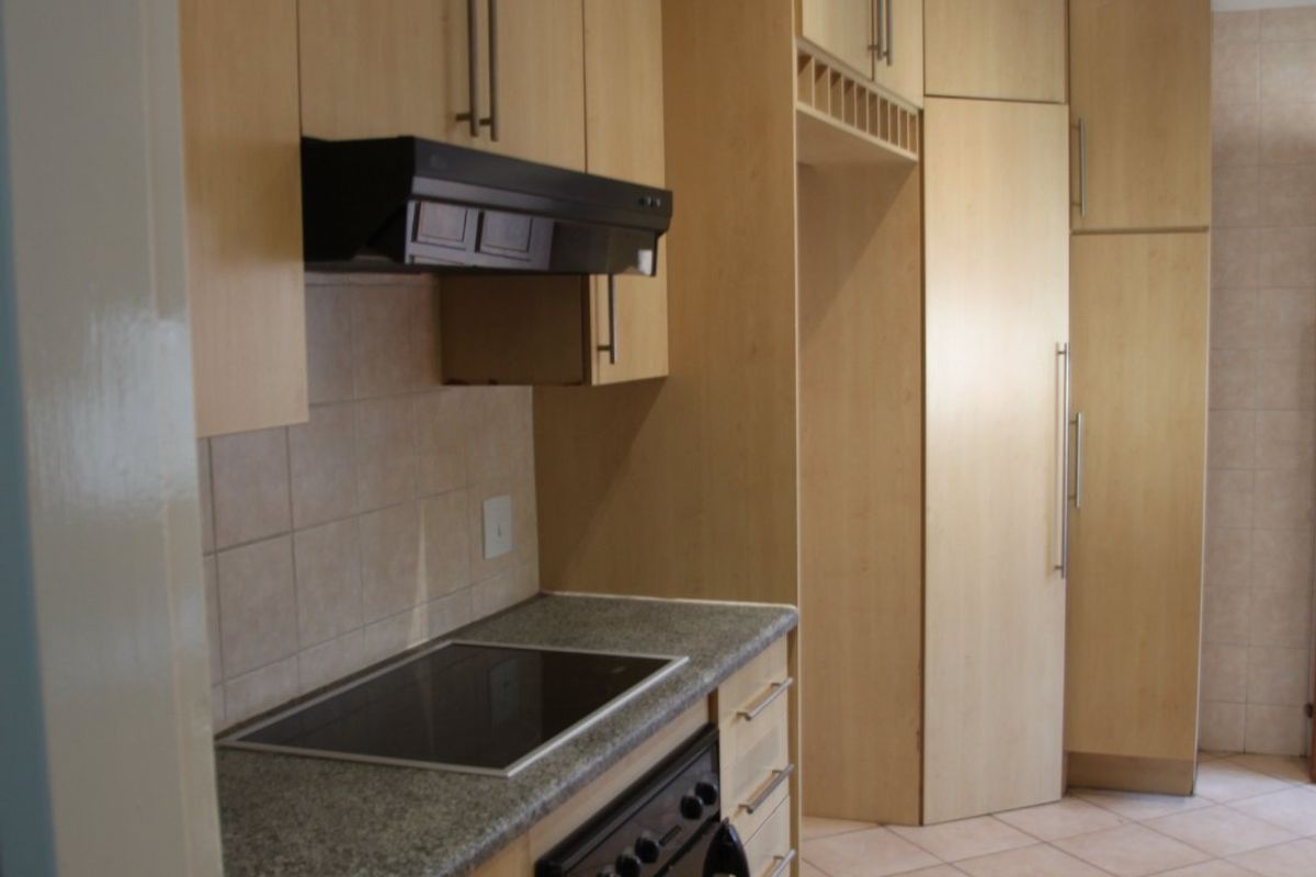 A clean, functional kitchen featuring light wood cabinetry, stone countertops, integrated appliances, and neutral tiled flooring.
