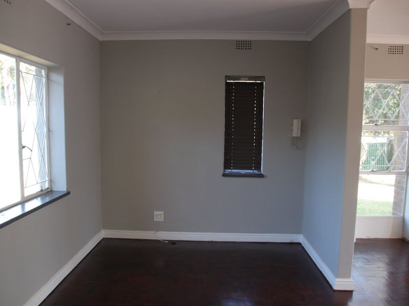 An empty living area featuring dark parquet flooring, neutral grey walls, and security bars on the windows, offering a clean and versatile space.