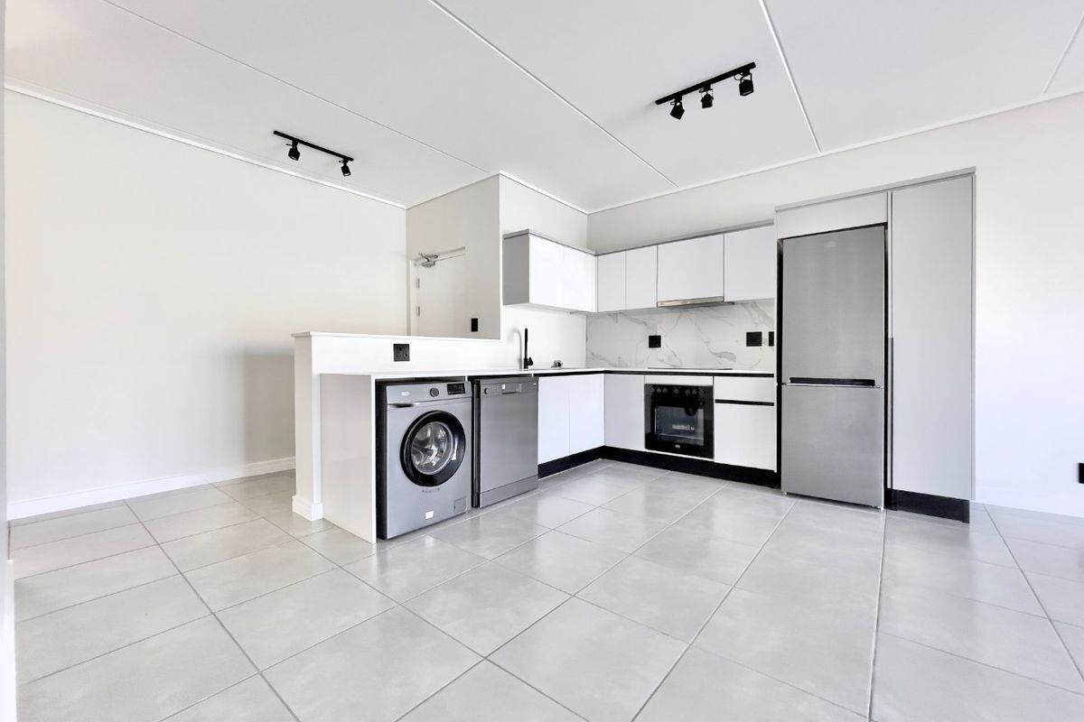Modern open-plan kitchen featuring sleek white cabinetry, marble-look splashback, tiled flooring, and integrated appliances including an oven and extractor fan.