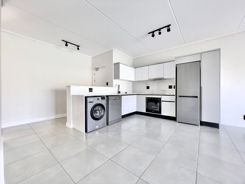 Modern open-plan kitchen featuring sleek white cabinetry, marble-look splashback, tiled flooring, and integrated appliances including an oven and extractor fan.