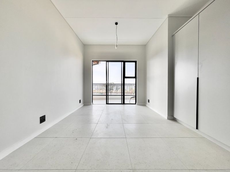 A bright, empty bedroom featuring modern tiled flooring, built-in cupboards, and a sliding glass door leading to a balcony.