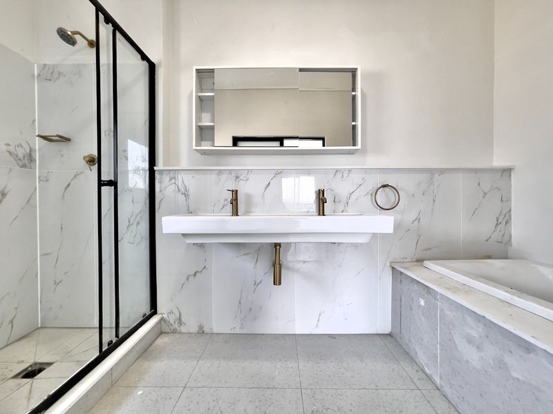 Modern bathroom featuring a double vanity, wall-mounted mirror cabinet, walk-in shower with glass enclosure, and a built-in bathtub with marble-look wall tiles.