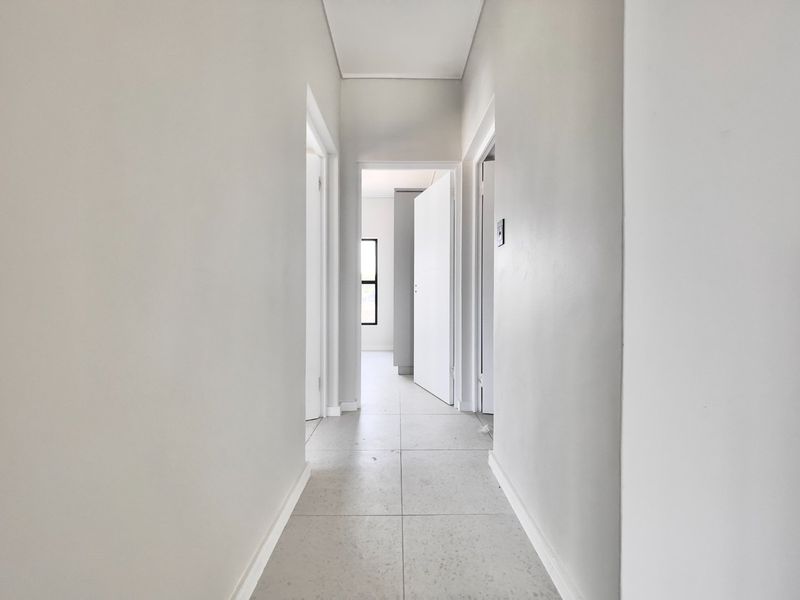 A clean, minimalist hallway featuring neutral wall finishes and light-colored floor tiles, providing access to multiple rooms within the apartment.