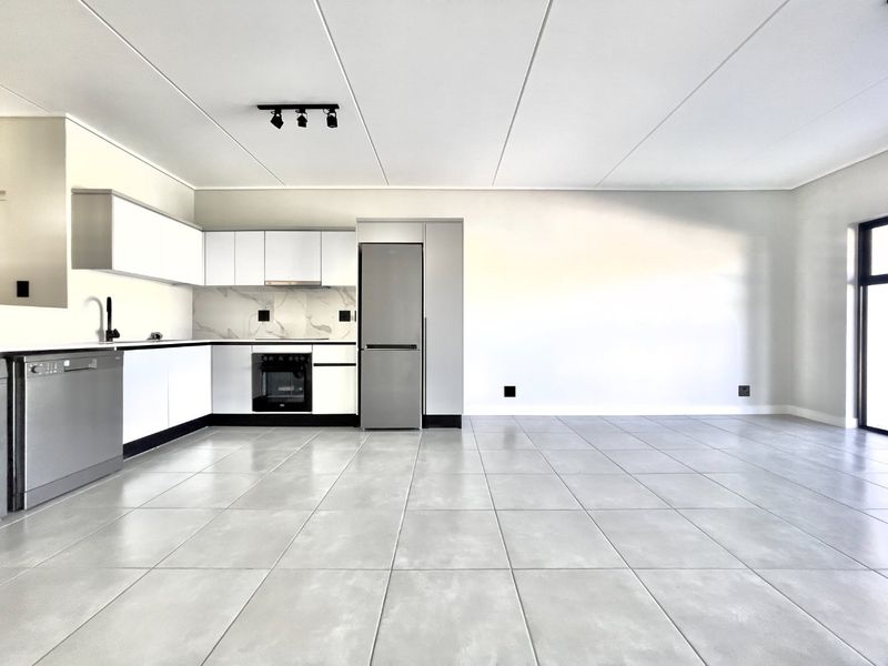 Modern open-plan kitchen and living area featuring sleek white cabinetry, integrated appliances, marble-look splashback, and neutral tiled flooring in a bright, spacious layout.