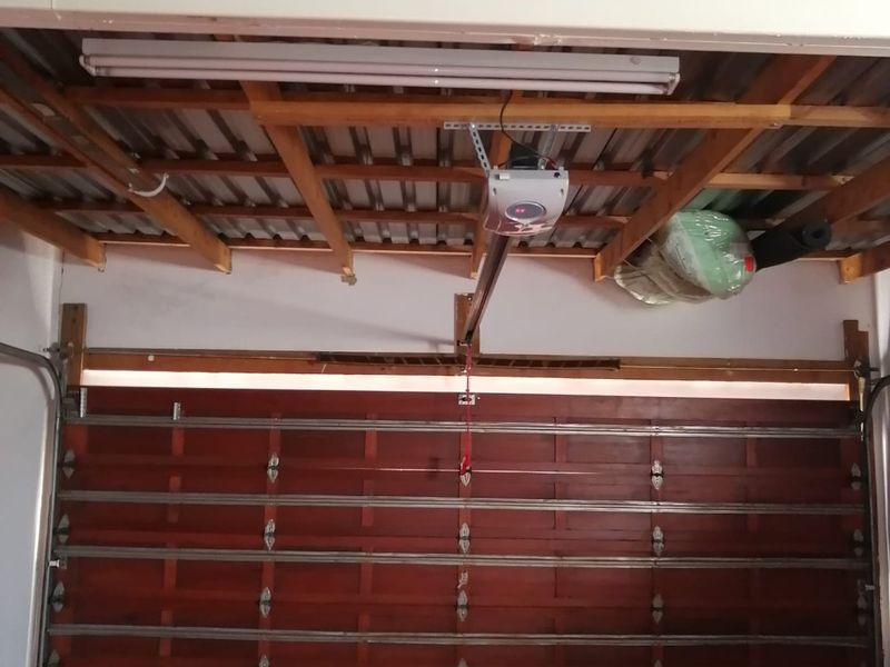 Interior view of a garage featuring a sectional timber door, automatic opener, and exposed roof structure with corrugated metal sheeting.