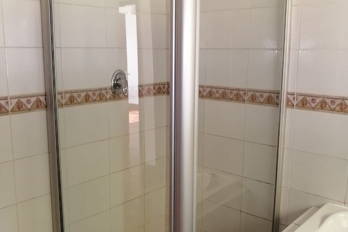 A functional bathroom featuring a corner shower enclosure with a metal frame and a built-in bathtub with tiled surround.