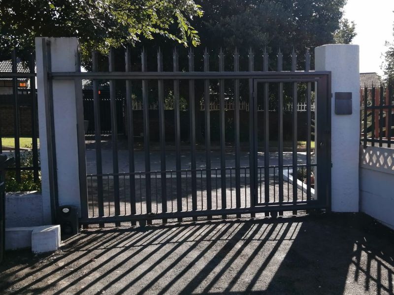 A secure metal entrance gate mounted between concrete pillars, providing access to the property driveway.