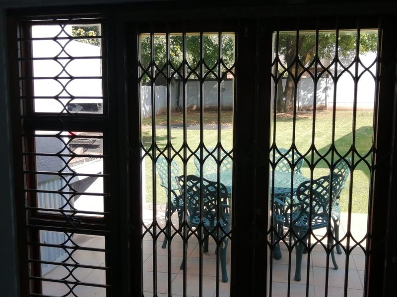 View from inside looking out through a security gate onto a paved patio area with garden access.