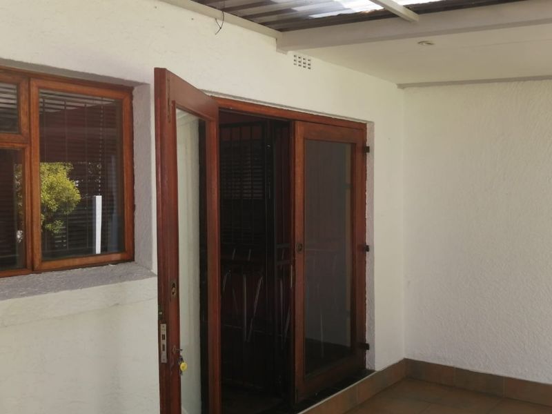 A covered patio area featuring tiled flooring, timber-framed glass doors, and a translucent roof, providing a functional outdoor transition space.