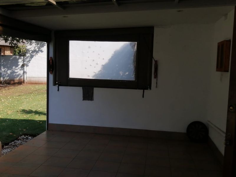 A covered outdoor patio area featuring tiled flooring and a translucent roof, providing direct access to the garden.