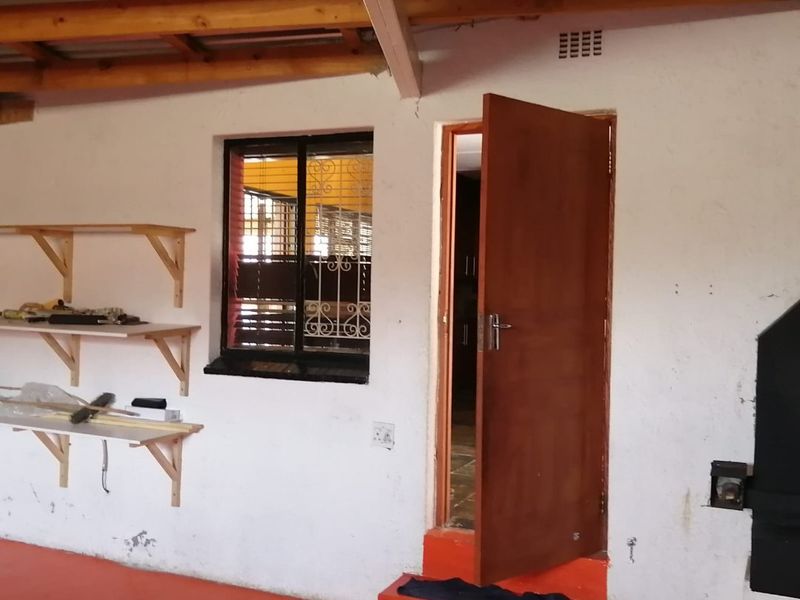 A functional garage space featuring exposed timber roof trusses, painted concrete flooring, built-in wall shelving, and a raised step leading to an internal doorway.