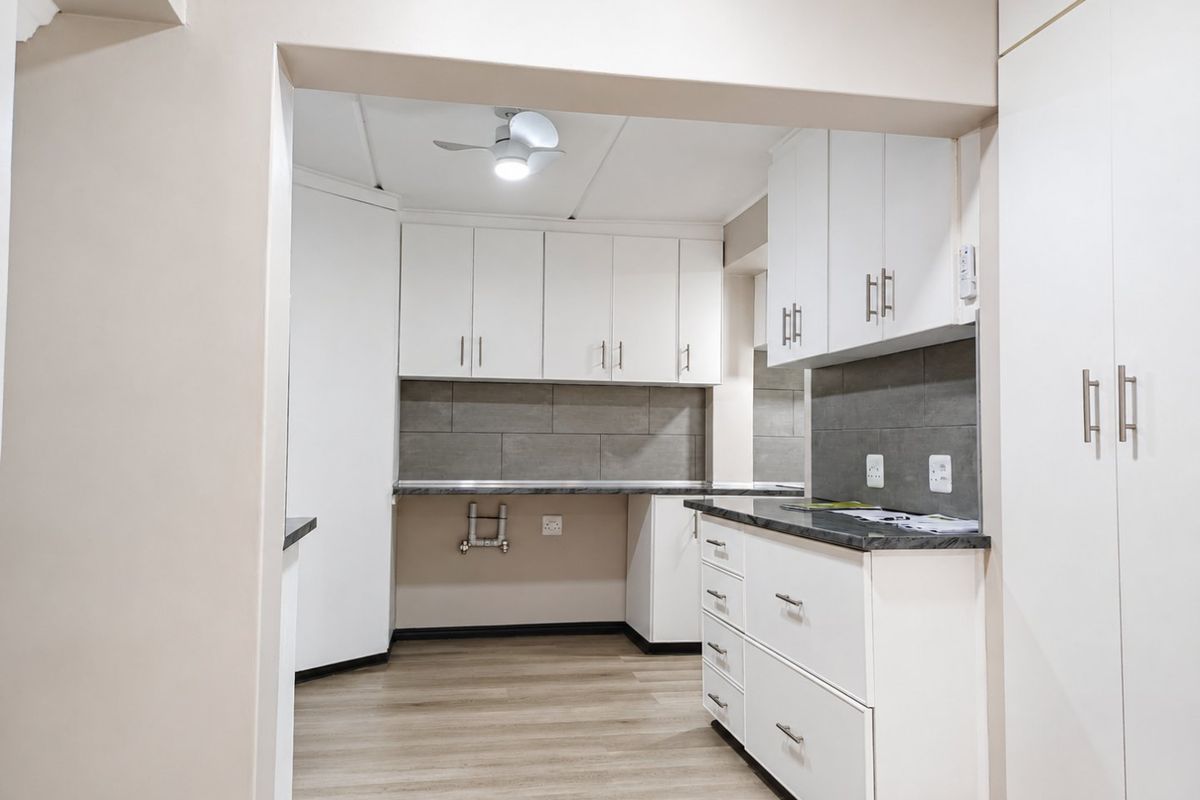 A clean, modern kitchen area featuring white built-in cabinetry, grey tiled backsplash, laminate countertops, and wood-look flooring.