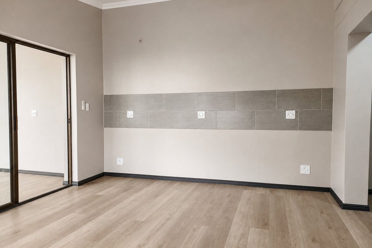 A bright, empty bedroom featuring modern laminate flooring, a tiled wall accent, and a sliding glass door leading to an outdoor area.