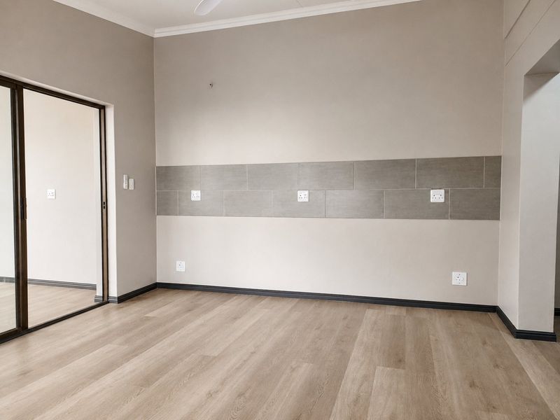 A bright, empty bedroom featuring modern laminate flooring, a tiled wall accent, and a sliding glass door leading to an outdoor area.