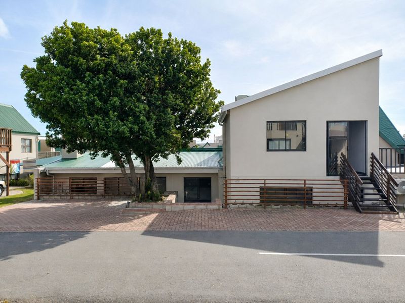 Front exterior view of the property featuring a paved driveway, metal staircase, and modern pitched roof design with established tree.