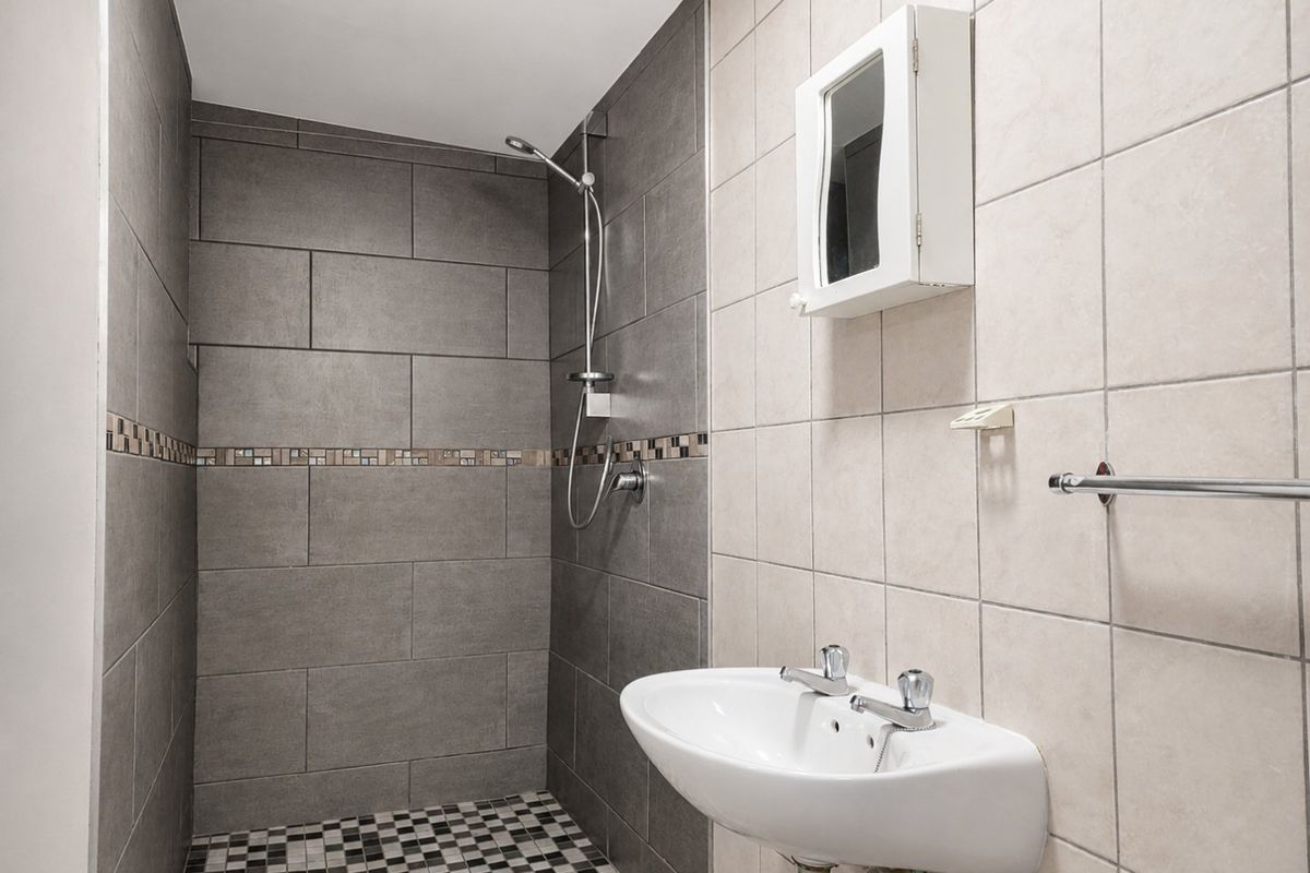 A functional bathroom featuring a walk-in shower with grey tiling, a wall-mounted basin, and a mosaic-tiled floor.