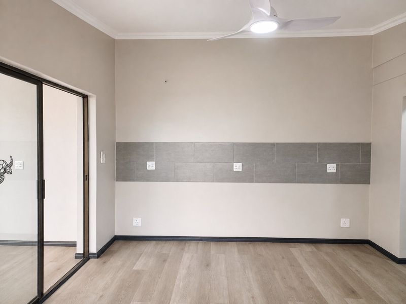 A bright, empty bedroom featuring modern laminate flooring, a ceiling fan, and a decorative tiled wall accent with integrated electrical outlets.