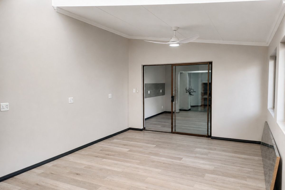 A bright, empty living area featuring modern laminate flooring, a ceiling fan, and a sliding glass door leading to an adjacent room.