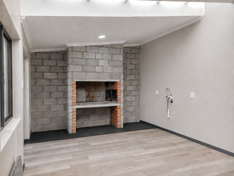 A clean, covered patio area featuring a built-in brick braai, skylight, and modern laminate flooring, ready for outdoor entertaining.