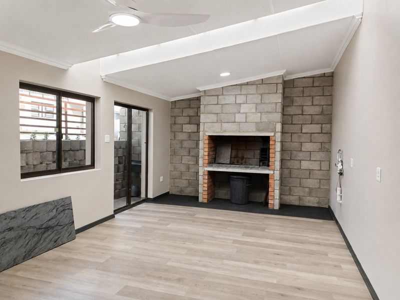 A spacious, covered patio area featuring a built-in brick braai, modern laminate flooring, and a ceiling fan, perfect for outdoor entertaining.