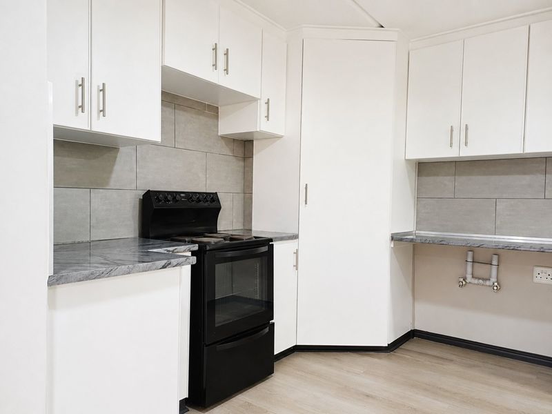 A clean, modern kitchen featuring white cabinetry, grey stone-look countertops, a grey tiled backsplash, and a black freestanding oven.