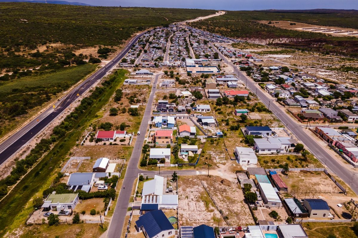 An aerial view of a residential neighborhood showing various plots, paved road infrastructure, and surrounding landscape.