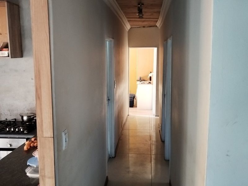 A narrow hallway featuring a timber-paneled ceiling and tiled flooring, providing access to adjacent rooms and a partial view into the kitchen area.
