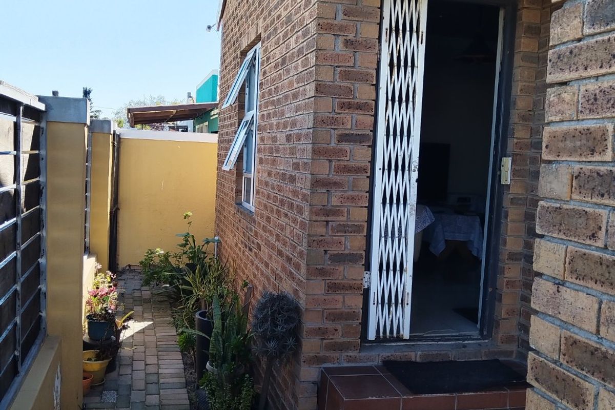A side view of the property featuring a face brick exterior, tiled entrance steps, a security gate, and a paved walkway along the boundary wall.