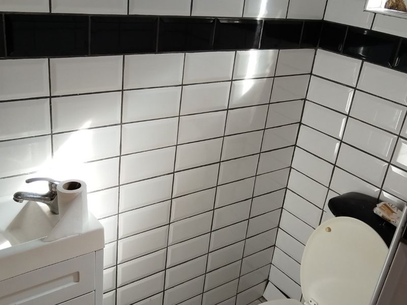 A compact bathroom featuring white subway wall tiles with a black accent border, a small vanity basin, and a toilet.