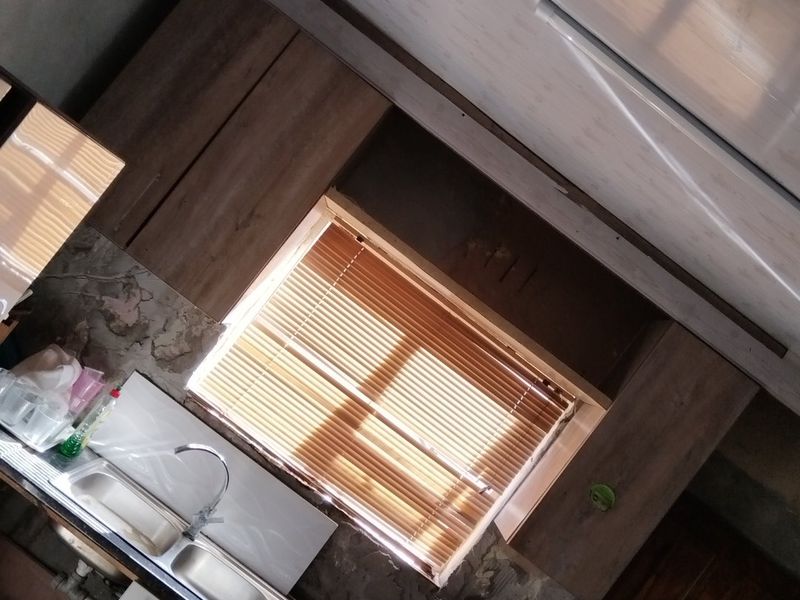 A kitchen area featuring cabinetry, a stainless steel sink, and venetian blinds, currently requiring wall repairs and finishing to complete the space.